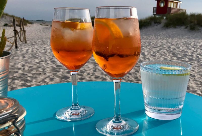 Falsterbo Vinglas 32cl från Barcompagniet. Här med 2 glas med Aperol & Spritz på stranden i Skanör. På bordet ser ni även Stripe 355 R med vatten.
